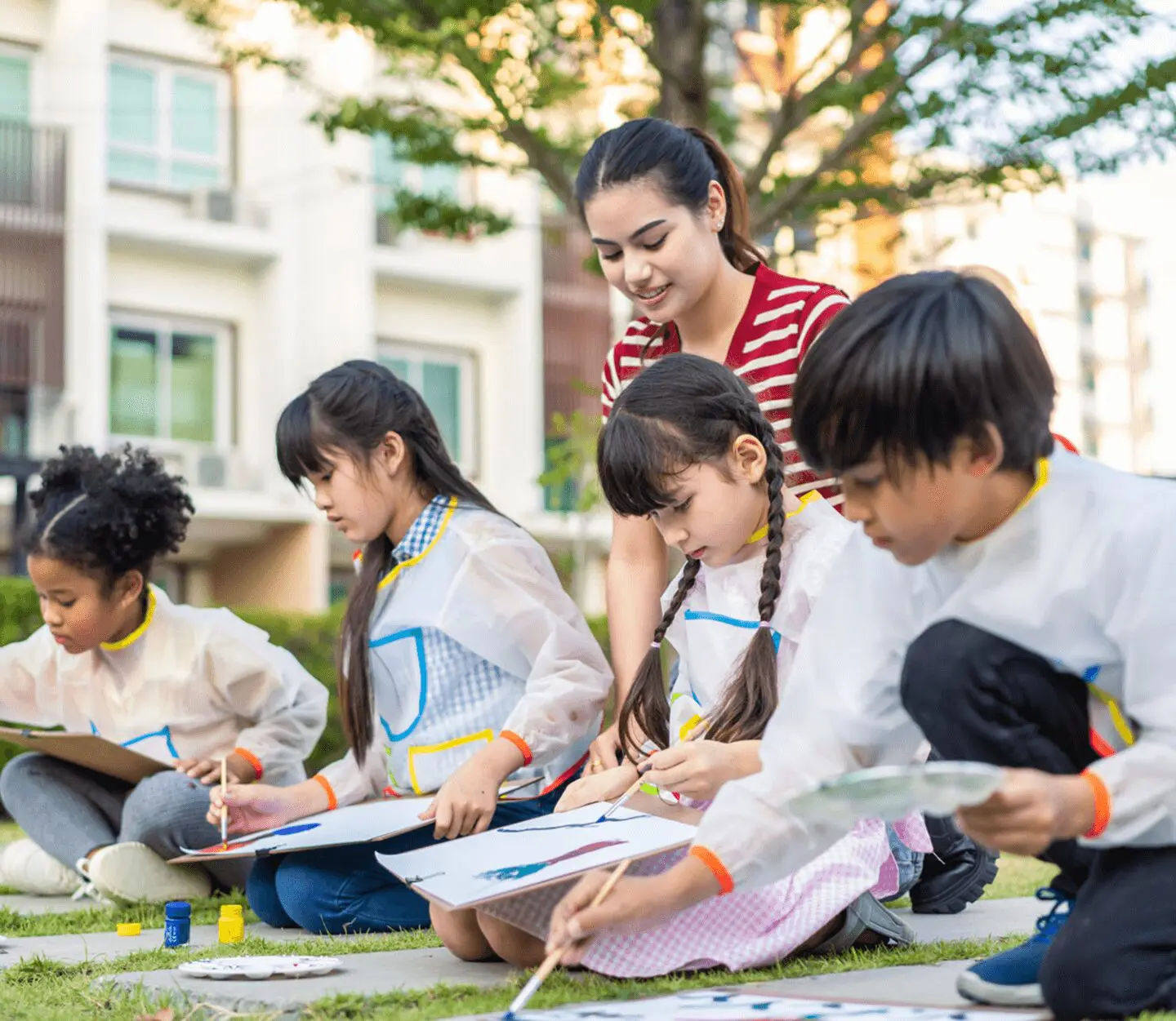 Children painting outdoors with a teacher's guidance.