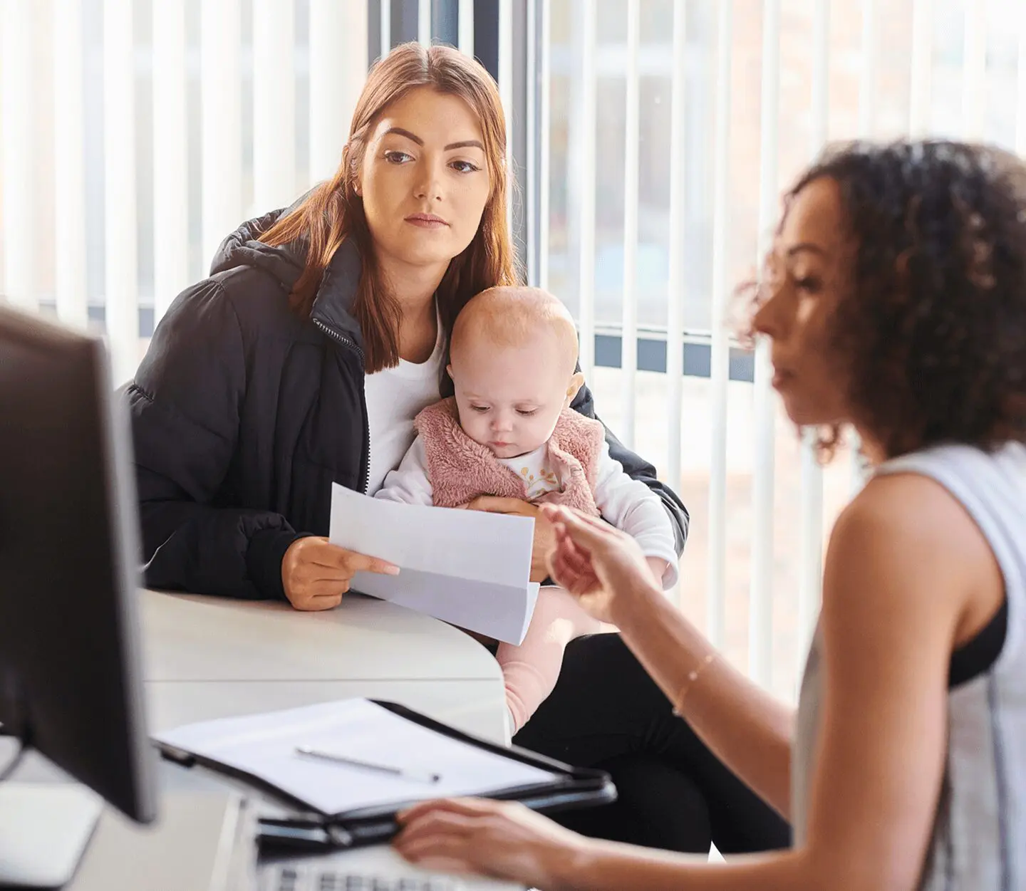 Woman with baby consulting another woman at desk.